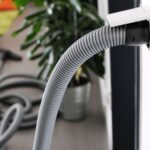 Central vacuum hose and attachment plugged in in home with hardwood floors.